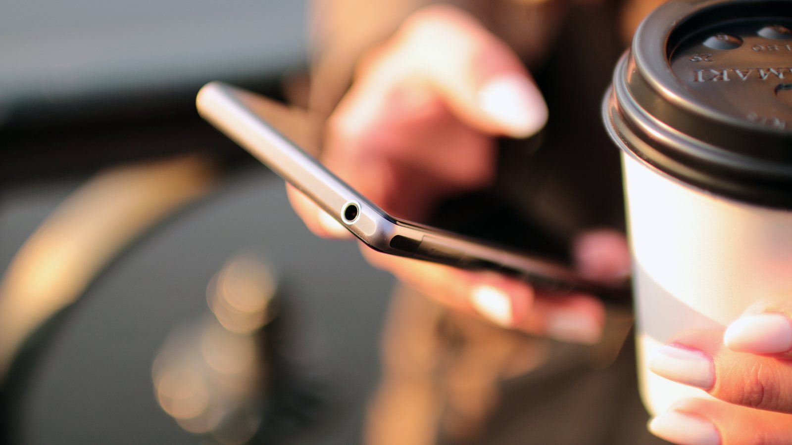 Dłonie trzymające smartfon i kubek kawy