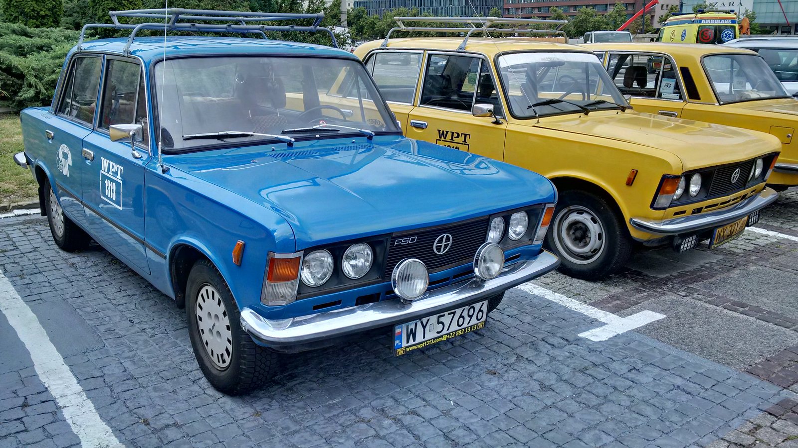 Polski Fiat 125p w kolorze niebieskim i żółte taksówki z czasów PRL na parkingu